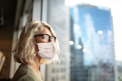 Mature-businesswoman-looking-out-of-window-with-face-mask