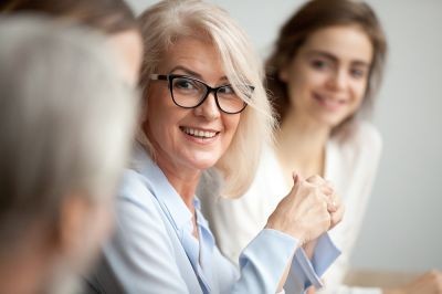 Smiling-aged-businesswoman-looking-listening-to-colleague-at-team-meeting-stock-photo
