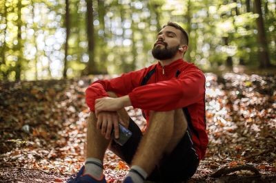 Portrait-of-relaxed-young-man-with-bluetooth-headphones-in-forest